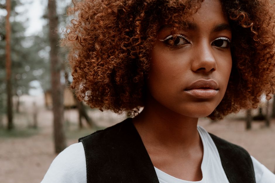 A striking portrait of a young woman with curly hair set against a natural forest backgrou