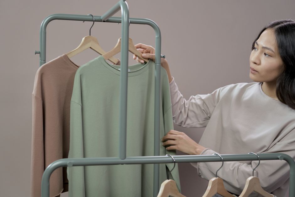 An Asian woman examines sweaters on a clothes rack in a fashion store.