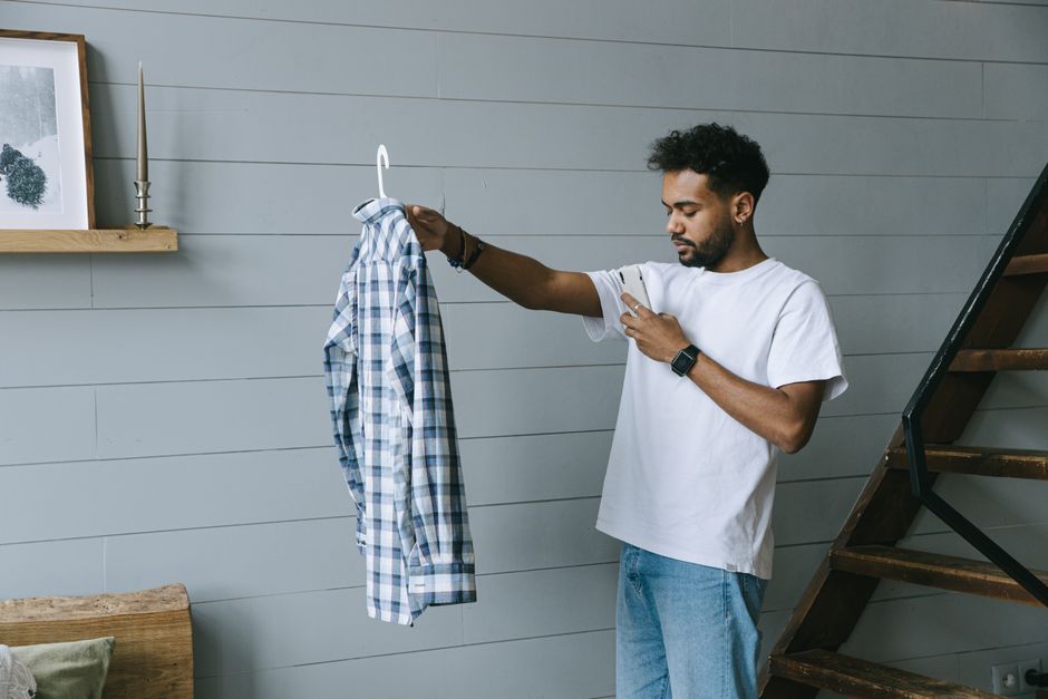 Young man taking photo of a plaid shirt indoors, showcasing fashion and casual style.
