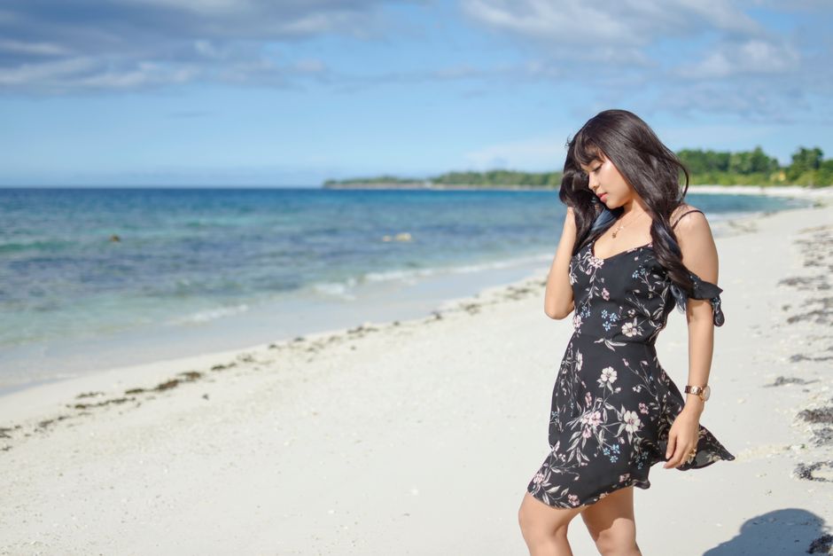 A woman stands on the sunny Namlea beach, Maluku, in a floral dress, enjoying the peaceful seashore.