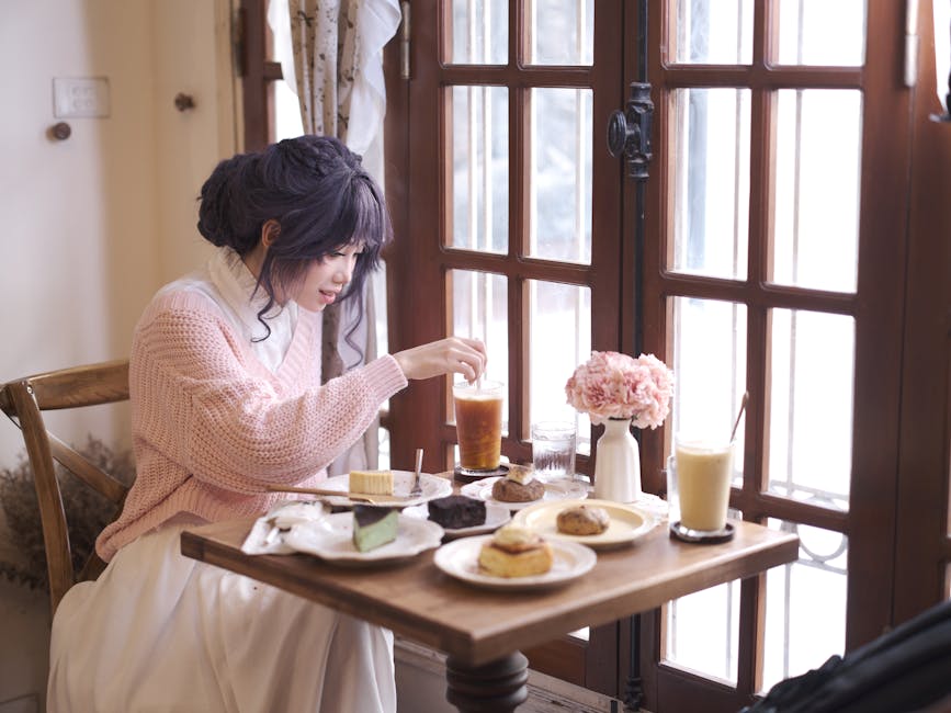 A serene scene of a woman enjoying afternoon tea with desserts by a window in a cozy setting.