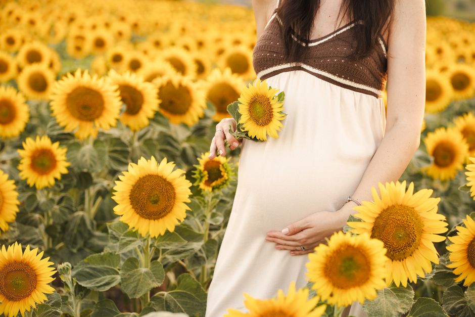 Beautiful pregnant woman holding sunflowers in a vibrant field, radiating joy and maternity glow.
