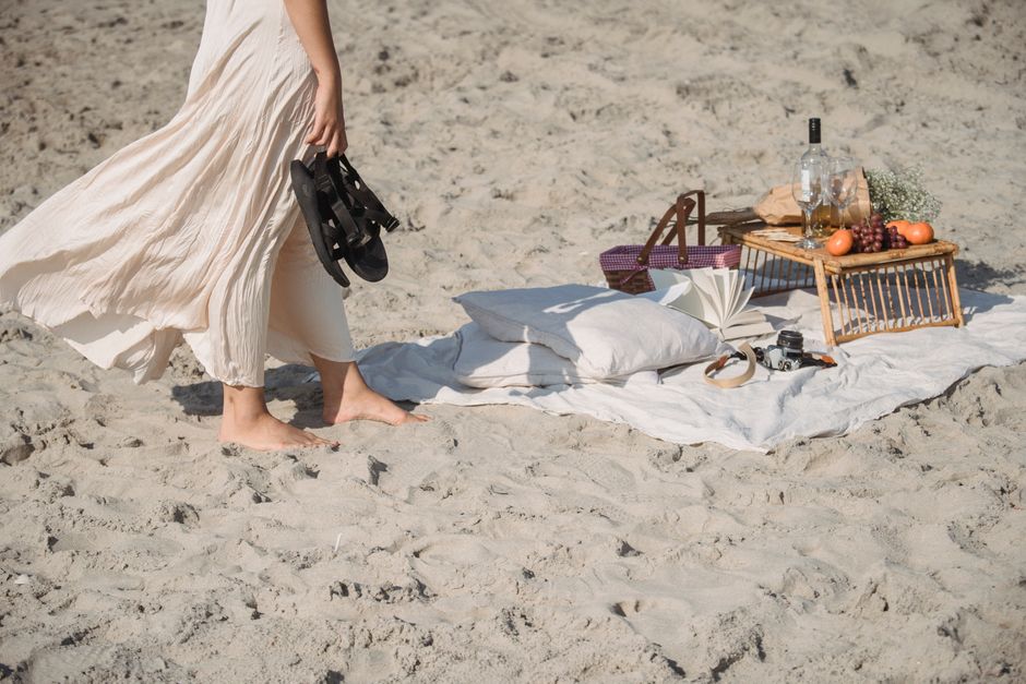 A tranquil beach picnic setup with a person enjoying a barefoot stroll by the shore.