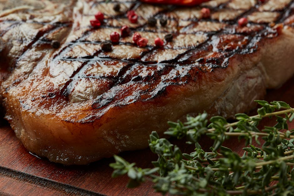 Close-up of succulent grilled ribeye steak with peppercorn and fresh thyme on a wooden board.