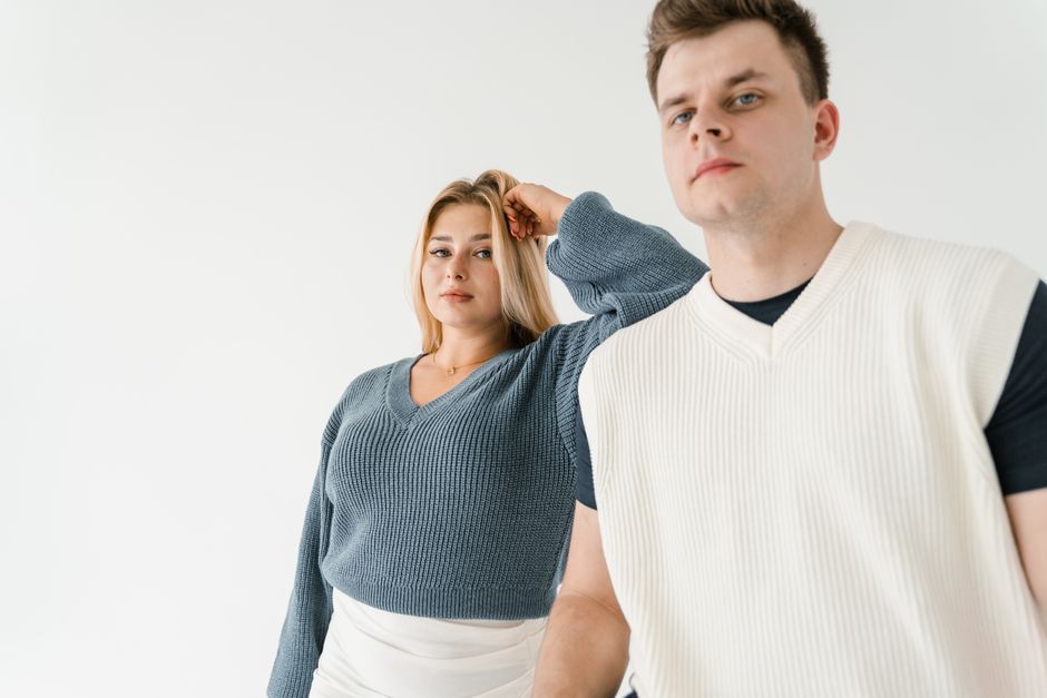 Two adults posing in a minimalist studio with stylish knitwear, showcasing fashion and confidence.