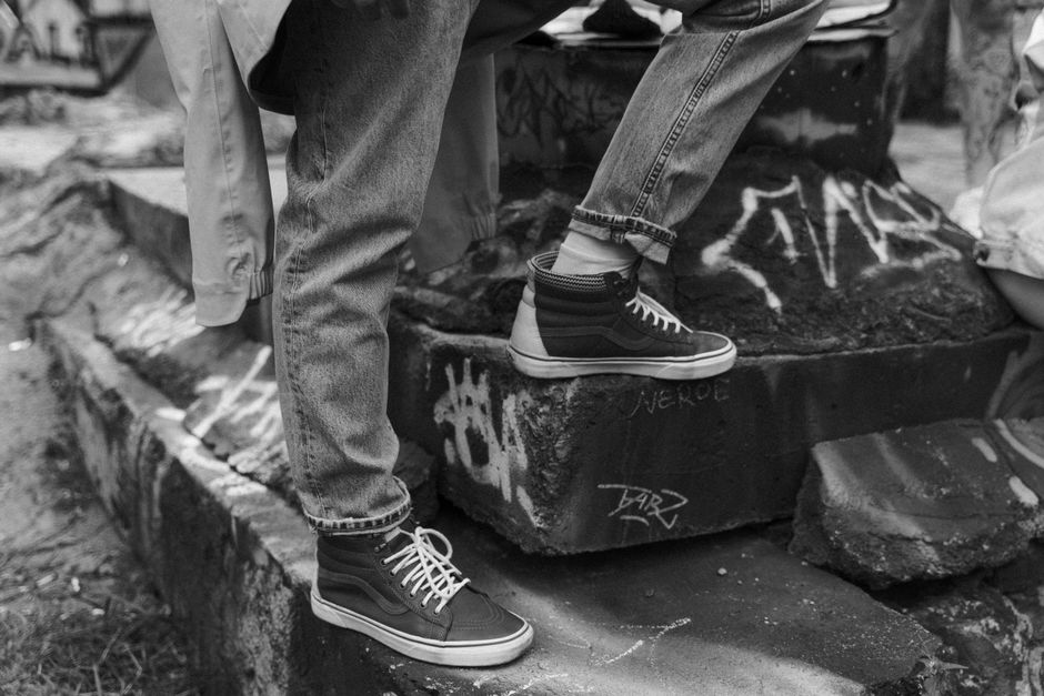 Black and white photo of denim jeans and sneakers amidst urban graffiti.
