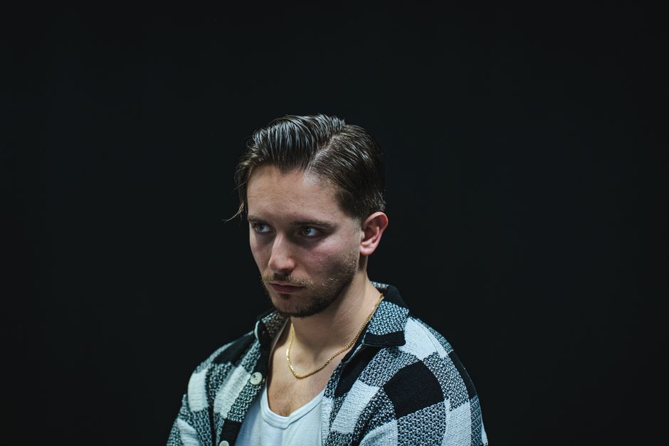 Dramatic studio portrait of a man wearing a checkered shirt against a dark background.