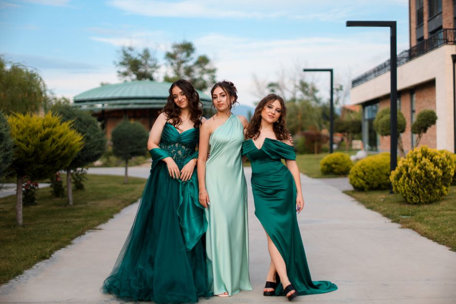 Three women in elegant green dresses standing on a sidewalk in an urban outdoor setting.