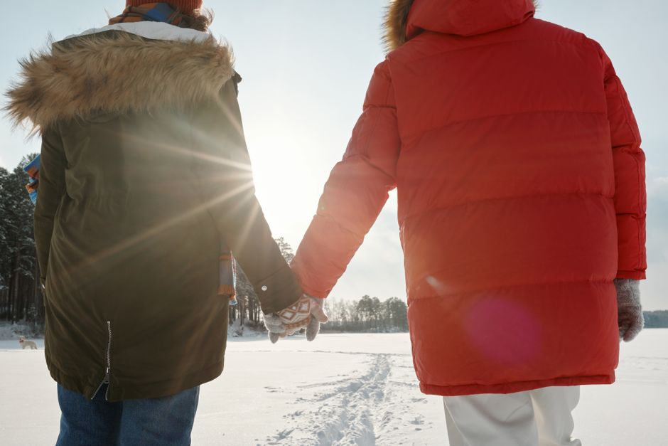 Couple walking on snowy path holding hands, showcasing winter togetherness.