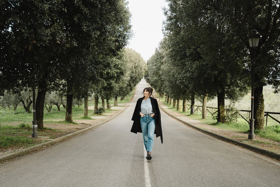 A woman strolls down a picturesque, tree-lined road in Tuscany, capturing a serene yet stylish moment.