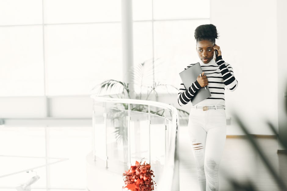 Young African American businesswoman talking on her phone while holding a laptop indoors.