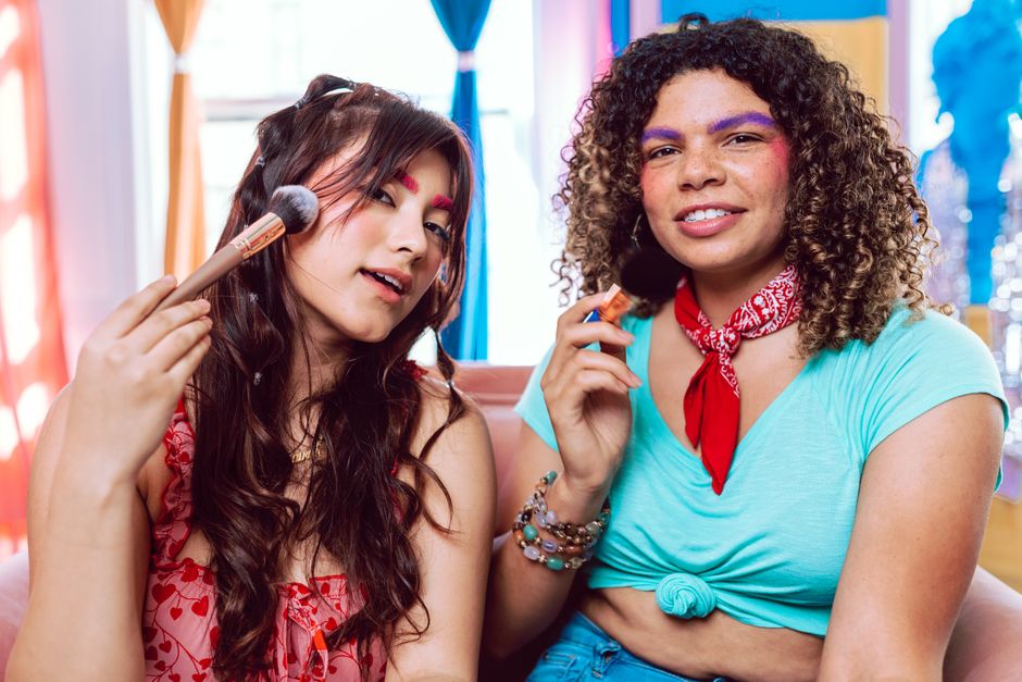 Two friends having fun with makeup brushes in a bright indoor setting, showcasing friendship and creativity.
