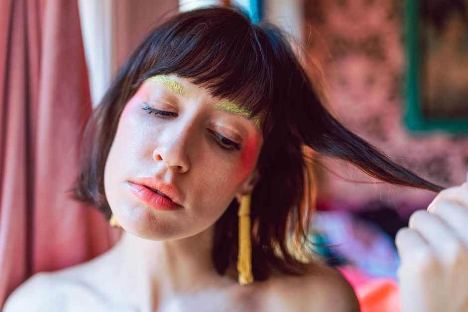 A fashion-forward young woman with colorful makeup indoors.