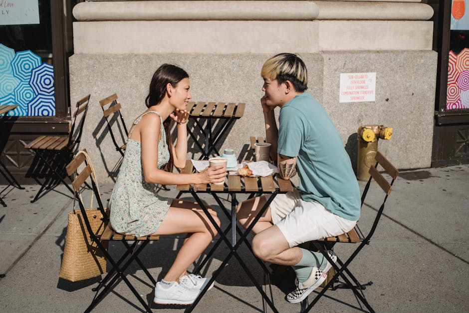 Side view of young multiracial couple looking at each other and drinking coffee on street on sunny day