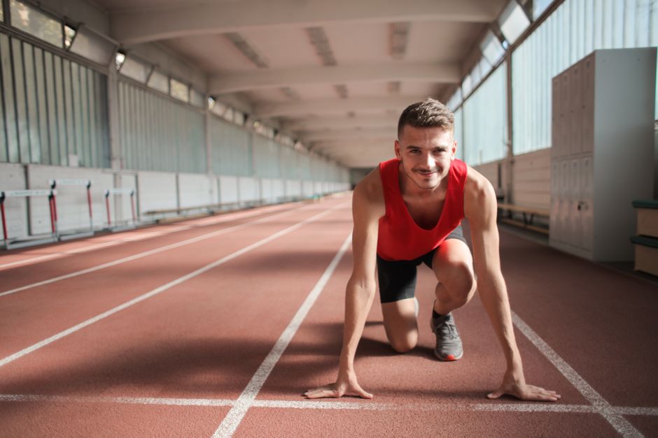 Male athlete in red top preparing for a sprint on an indoor track, showcasing determination and focus.