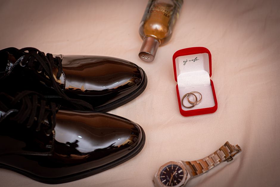 Stylish men's wedding accessories including shoes, rings, a watch, and a cologne bottle on a soft background.