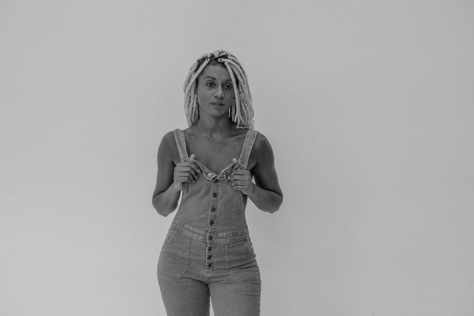 Black and white portrait of a woman in overalls with dreadlocks shot in a studio.