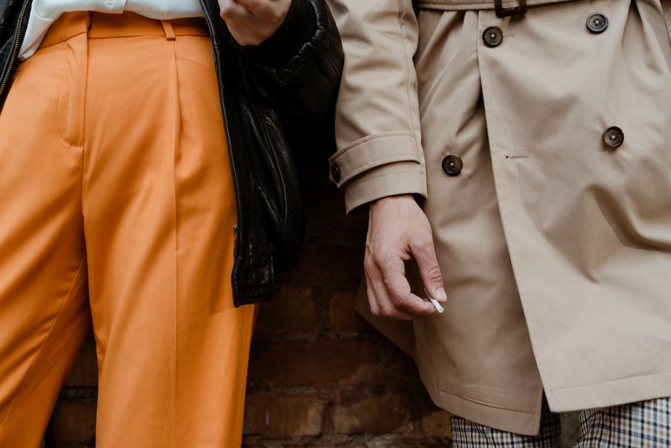 Chic street fashion featuring a beige trench coat and vibrant orange pants, close-up view.