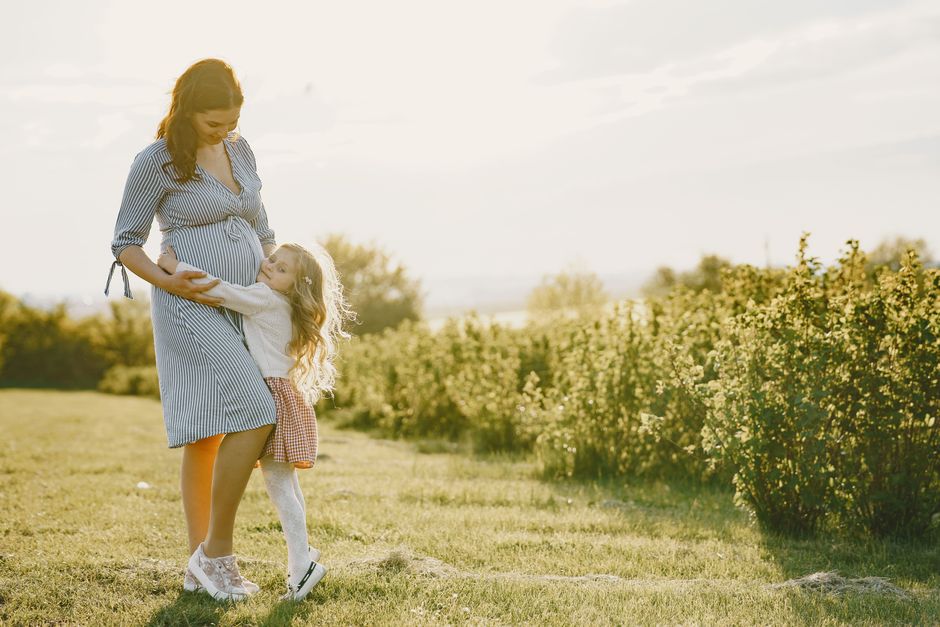 A loving moment between a pregnant mother and her daughter in a sunny field.