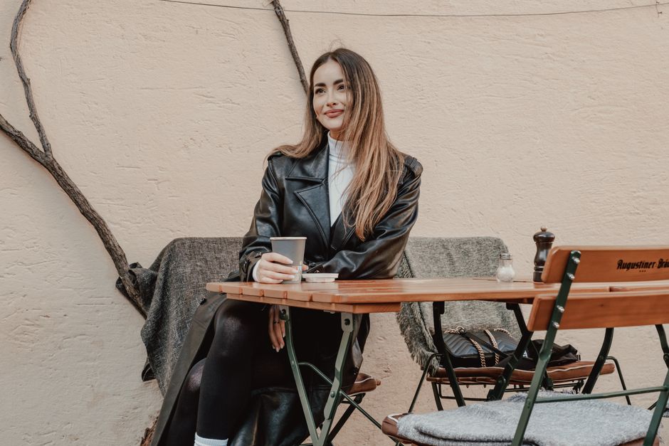 A stylish woman in a leather coat enjoying coffee at an outdoor cafe table, exuding elegance.