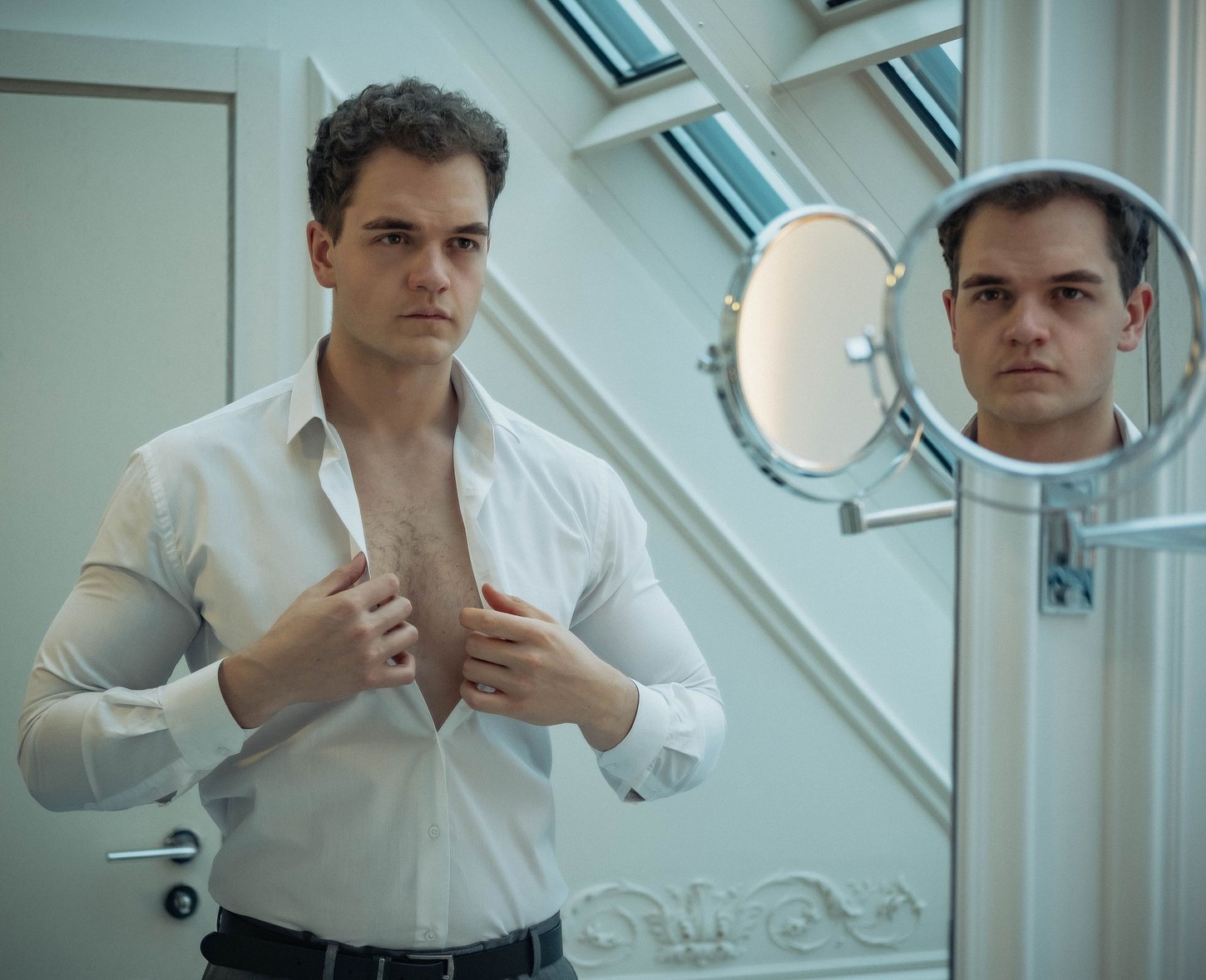 Man buttoning a white shirt in front of a mirror