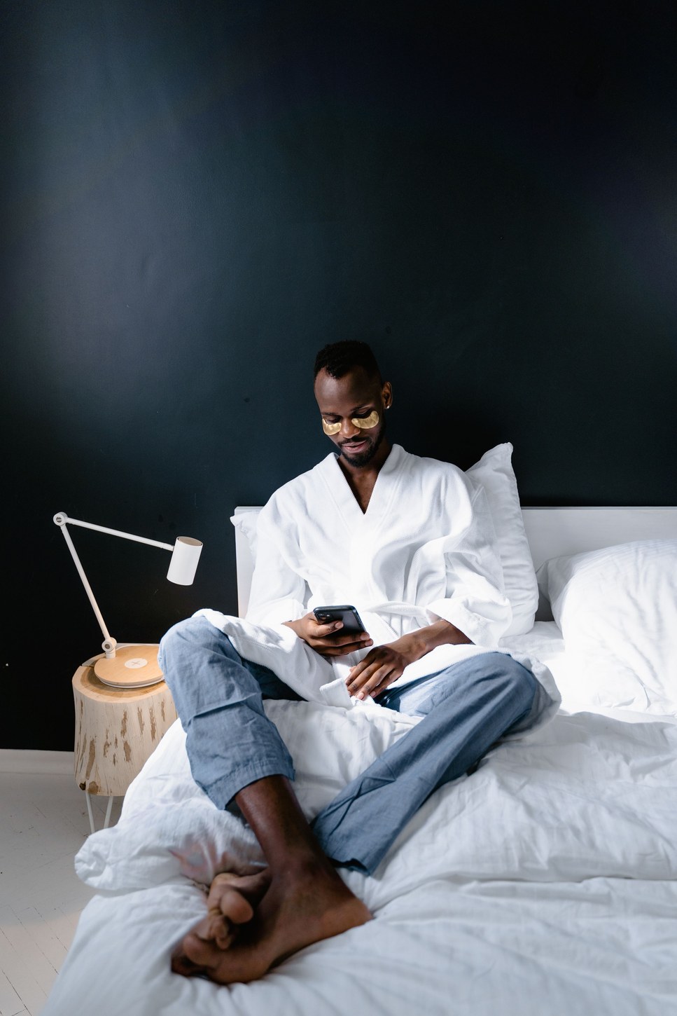 Man in a robe relaxing on a bed with under eye patches