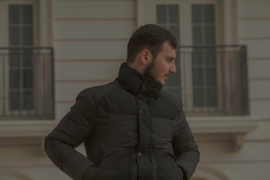 Portrait of a man in a black jacket standing outdoors against an urban background.