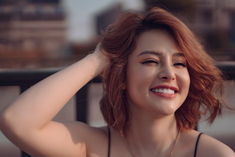 Positive young lady with short ginger hair touching hair with hand and looking away in sun