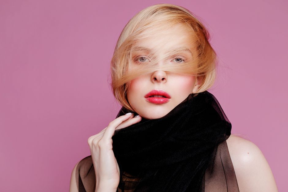 Stylish portrait of a woman wearing a black scarf with pink background, showcasing eleganc