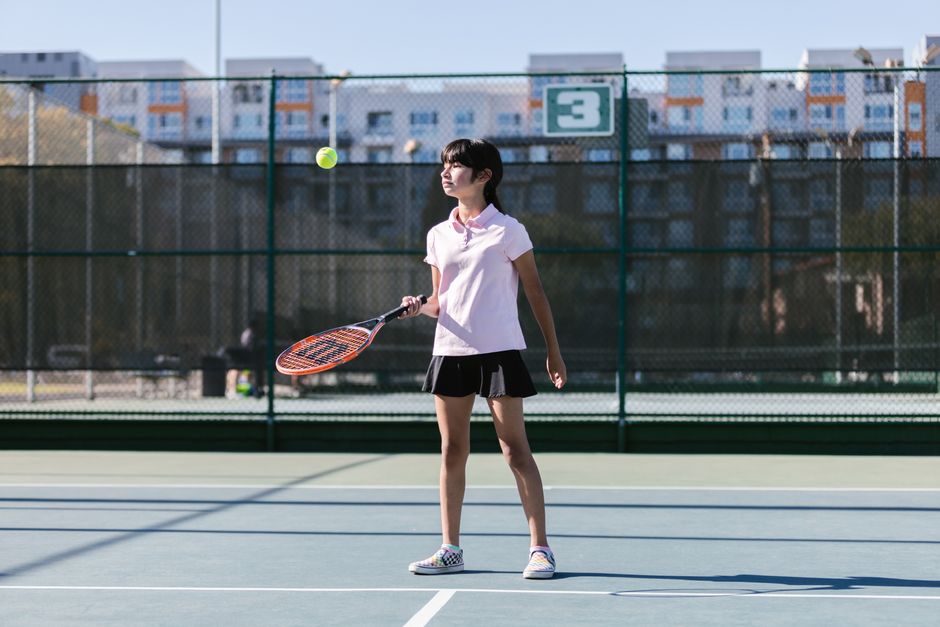 A young girl in sportswear practicing tennis outdoors on a sunny day.