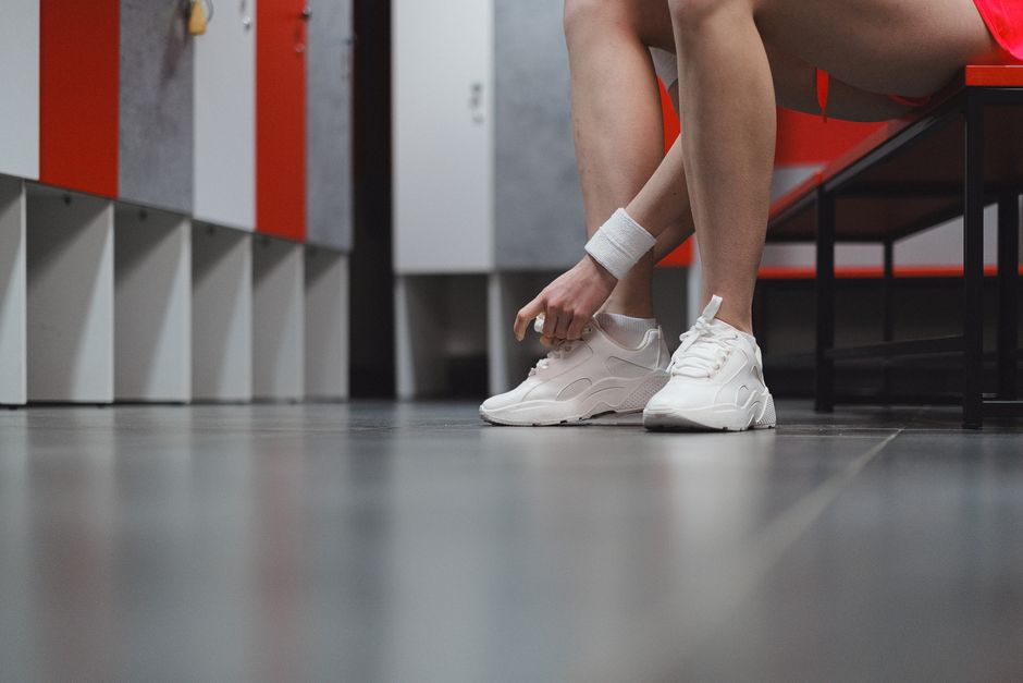 Female athlete tying white sneakers in a gym locker room, ready for exercise.