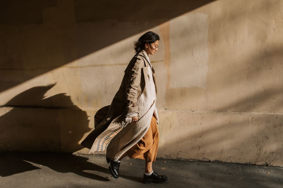 Side view of a stylish woman in a trench coat walking in sunny autumn weather.
