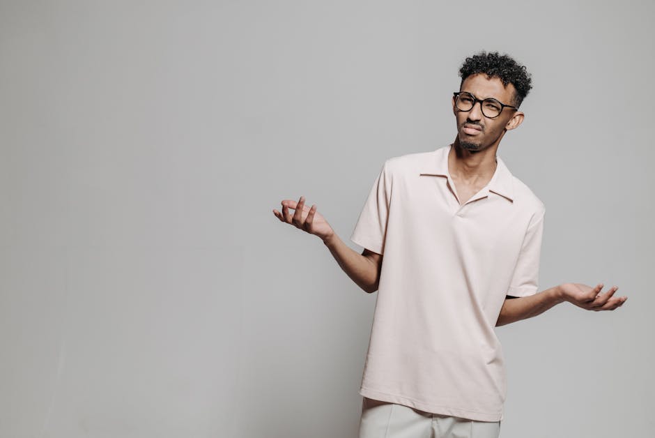 Studio portrait of a young African American man wearing eyeglasses and a white polo shirt expressing confusion.
